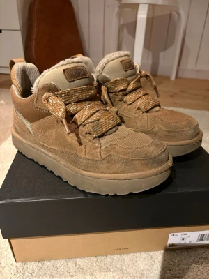 Beige sneakers från UGG med teddyfoder - Snygga sneakers från UGG i beige mocka och textil med grova mönstrade snören och mjukt teddyfoder. Skorna har en chunky sula och UGG-logga på plösen. Perfekta för dig som vill ha både stil och komfort.