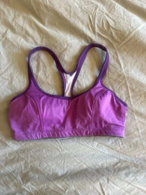 Lila sport-bh från Champion - Sport-bh från Champion i lila med kontrasterande mörklila kant. Bh:n har brottarrygg och är tillverkad i ett stretchigt material som ger medium support. Perfekt för träning och aktiva dagar. Motsvarar xs/s 