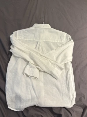 Vit linneskjorta från Lyle & Scott - Klassisk vit skjorta i linne från Lyle & Scott med lång ärm och knappar framtill. Skjortan har en gul broderad logga på bröstet och en avslappnad passform. Perfekt för en stilren och fräsch look. Pris kan diskuteras