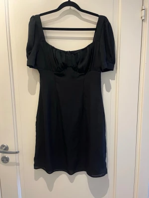 Svart klänning S - Stilren svart klänning med puffiga ärmar och fina detaljer från NA-KD. Klänningen har en figurnära passform som ger en elegant känsla. Perfekt för dig som gillar en enkel men elegant look.