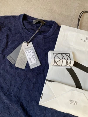 Mörkblå ulltröja från Ferrante - Säljer en elegant mörkblå tröja från Ferrante, tillverkad i 100% extra fin merinoull. Känns som ett andra lager hud. Tröjan har ett subtilt mönster och långa ärmar, perfekt för kyligare dagar. Tillverkad i Italien för högsta kvalitet.  Prislappar, och kvitto från NK ingår vid köp.  