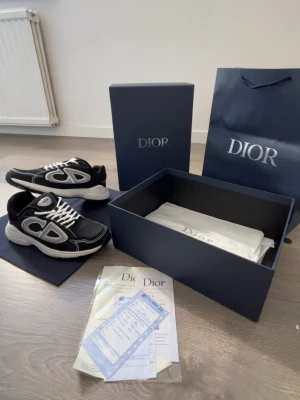 Svarta Dior B30 sneakers med vita detaljer - Säljer ett par svarta Dior B30 sneakers med vita och grå detaljer samt stora CD-loggor på sidorna. Skorna har en chunky vit sula, mesh och läderpaneler samt vita skosnören. Kommer med originalkartong, dustbag och Dior-påse.