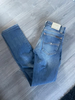 Blå jeans från Nudie Jeans - Snygga blå jeans från Nudie Jeans med klassisk femficksdesign och ljusare slitningar. Jeansen har kontrastsömmar och den ikoniska vågade brodyren på bakfickan. Tillverkade i mjuk denim med en avslappnad passform.
