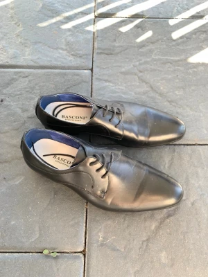 Svarta loafers från Basconi - Stilrena svarta loafers från Basconi i slätt läder med klassisk snörning och diskret blå insida. Snygg, smal tåform som passar perfekt till en dressad look. Perfekta skor för dig som gillar en clean och tidlös stil. Använda en gång 