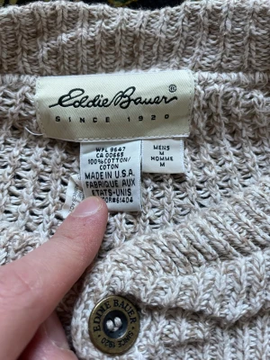 Beige stickad tröja från Eddie Bauer - Snygg beige stickad tröja från Eddie Bauer i 100% bomull. Tröjan har långa ärmar, ribbstickade muddar och en knappslå med fyra knappar framtill. Perfekt för dig som gillar klassisk och avslappnad stil.