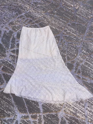 Vit långkjol med spetsdetaljer - Säljer en vit långkjol med vacker spets och asymmetrisk nederkant. Kjolen har flera våder och ett diskret mönster i spetsen som ger en romantisk känsla. Perfekt för dig som gillar en feminin och stilren look. Haft på mig den bara 1 ggn. Helt ny 