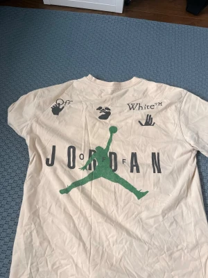Off-White x Jordan beige t-shirt - En officiell sällsynt Off White x Jordan t-shirt som säljs nypris på 800kr T-shirten är såklart äkta och är i storlek M. Tshirten är på en mycket bra skick men kräver endast strykning så är den som ny!