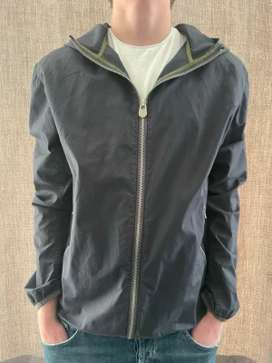 Svart vindjacka från Colmar - Stilren svart vindjacka från Colmar med dragkedja framtill och två sidofickor med dragkedja. Jackan har en diskret logotyp på vänster ärm och en lätt, smidig passform. Perfekt för blåsiga dagar och enkel att matcha med jeans eller hoodie.