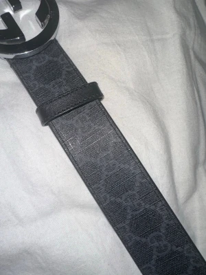 Svart Gucci bälte med GG-spänne - Snyggt svart bälte från Gucci med klassiskt GG-mönster och ett stort, rundat silverspänne med GG-logga. Bältet är gjort i skinn och har en stilren look som passar till många outfits.