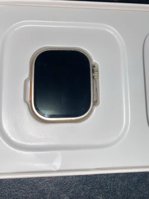 Apple Watch Ultra silverfärgad - Snygg Apple Watch Ultra med fyrkantig form och silverfärgat metallhölje. Stor och tydlig skärm med digital krona på sidan. Perfekt för dig som vill ha en smartklocka med modern design och avancerade funktioner.klockan är ej äkta