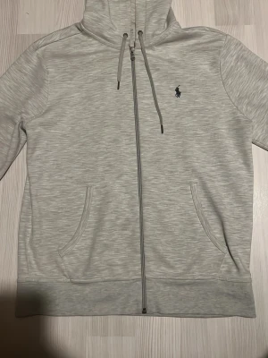  hoodie från Polo Ralph Lauren - Snygg ljusgrå hoodie med dragkedja från Polo Ralph Lauren. Köptes i room 1006, Klassisk design med två fickor fram, Tillverkad i mjukt och bekvämt material som passar perfekt till chill dagar.