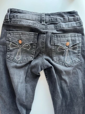 Grå jeans med broderade bakfickor - Säljer ett par grå jeans från Gina Tricot med snygga broderade detaljer på bakfickorna och kopparfärgade knappar. Jeansen har klassisk femficksmodell och raka ben. Materialet är mjukt denim i bomull med lite stretch för extra komfort.