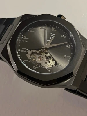 XoR Obsucra 41 mm Automatiskt urverk HELT NY - Snygg svart klocka från XoR watches med stainless steel armband och grå/svart urtavla. Klockan har ett öppet urverk som syns genom urtavlan och arabiska siffror i en unik design. Skickas med XoR original box.