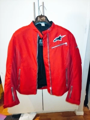 Röd Mcjacka dam från Alpinestars Stella - Ny Alpinestars Stella Gp-r MC-jacka (Dam) – Strl M Beskrivning: Säljer en helt ny och oanvänd Alpinestars Stella motorcykeljacka i en snygg röd färg. Jackan har en sportig slimmad passform och är utrustad för både högsta säkerhet och komfort. Slitstarkt textilmaterial Cordura Skydd: Fullt utrustad med inbyggda skydd för både armbågar och axlar, samt ryggskydd. Väder: Dubbelt foder som enkelt går att ta bort, vilket gör att jackan fungerar utmärkt både under varma och kyligare dagar. 