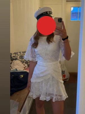 Studentklänning  - Säljer min Studentklänning 🥰Kort vit klänning med blommigt spetsmönster och volangdetaljer. Klänningen har halvlånga, lätt utsvängda ärmar och omlottliknande kjol. Stängs med dragkedja i ryggen.