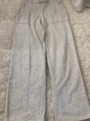 Grå mjukisbyxor - Säljer ett par ljusgrå mjukisbyxor med raka ben och bred resår i midjan samt dragsko. Byxorna har stora fickor framtill och är gjorda i mjukt sweatshirtmaterial. 