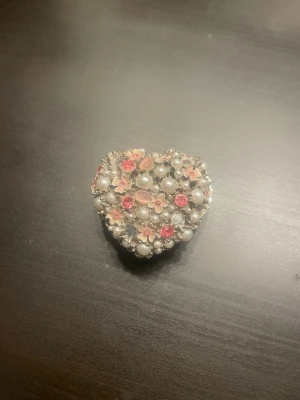 Hjärtformad smyckeask med pärlor - Söt hjärtformad smyckesask dekorerad med vita pärlor, rosa stenar och små blommor. Smyckesasken har en silvrig metallbas och gnistrar fint i ljuset. Perfekt ask för att förvara smycken och att ha på sminkbordet.
