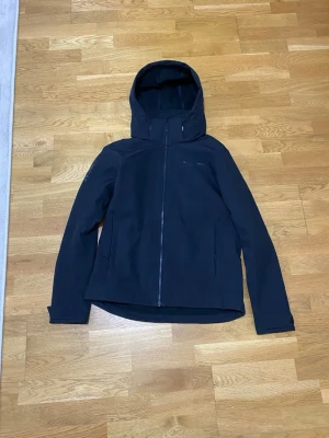 Svart vindjacka från Race Marine - Snygg svart vindjacka från Race Marine med hel dragkedja framtill och justerbar huva. Jackan har två sidofickor med dragkedja och diskret logga på bröstet. Tillverkad i ett mjukt och smidigt material som står emot vind.