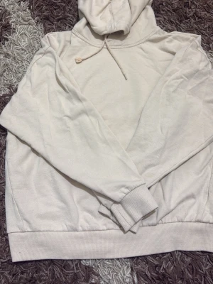 Beige hoodie från 157 med huva - Säljer en stilren beige hoodie från 157 med huva och dragsnören. Tröjan har ribbade muddar vid ärmslut och nederkant, och är tillverkad i mjukt material som känns skönt mot huden. Perfekt för dig som gillar en enkel och clean look.