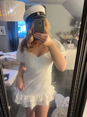 Vit kort klänning med volang - Supersöt vit broderad klänning med blommiga detaljer. Perfekt till studenten !!! Säljer då den är för kort på mig 