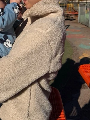 Beige teddyjacka med krage - Mysig beige teddyjacka med hög krage och avslappnad passform. Jackan är gjord i fluffigt teddy-material som håller dig varm och ger en trendig look. Perfekt för kyliga dagar och enkel att matcha med olika outfits.