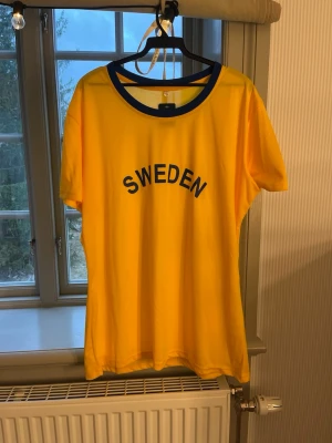 Svergietröja  - Gul t-shirt med blå rund halsringning och texten 'SWEDEN' tryckt på bröstet. Den är ny med prislapp. Använde under min inspark men dags att säljas. Det är bara att höra av er vid frågor!