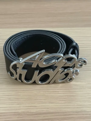 Svart Acne Studios skärp i skinn - Snyggt svart skärp från Acne Studios med bred rem i skinn och en stor, silverfärgad logotyp-spänne framtill. Perfekt accessoar för att lyfta din outfit med en cool detalj. Passar till jeans eller byxor för en trendig look. Skriv privat vid minsta fundering. Pris går att diskutera☺️