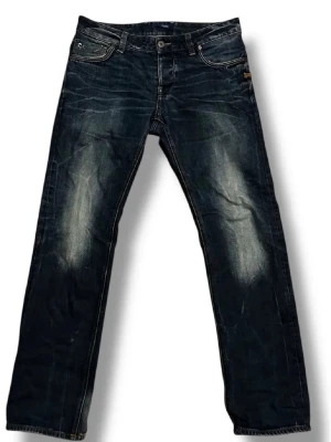 Mörkblå jeans från G-Star RAW - Säljer ett par mörkblå jeans från G-Star RAW med snyggt slitna detaljer och kontrastsömmar. Klassisk femficksmodell med raka ben och läderpatch bak i midjan. Perfekta för dig som gillar en avslappnad men ändå stilren look.
