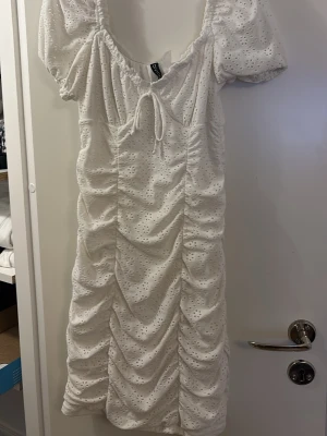 Vit broderad klänning med puffärm - Superfin vit klänning med broderade detaljer och puffärmar. Klänningen har snörning vid bysten, rynkade sidor och är tillverkad i bomull. Perfekt för sommarens alla tillfällen!