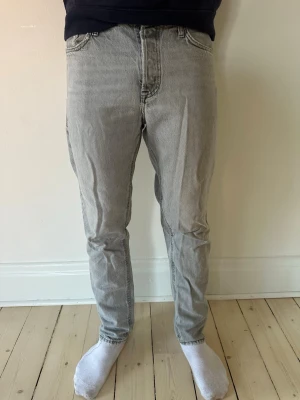 Jack and Jones jeans - Säljer ett par grå jeans med rak passform. Jeansen har klassiska fem fickor och synliga sömmar på bakfickorna. Materialet är denim i bomull och färgen är ljusgrå, perfekt för en avslappnad och trendig look.