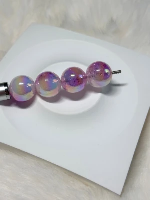 Iridescent lila glaspärlor 16 mm - Fyra runda glaspärlor i skimrande lila med inslag av rosa och blått. Pärlorna har en glansig yta och ett genomgående hål för smyckestillverkning. Funkar på penna