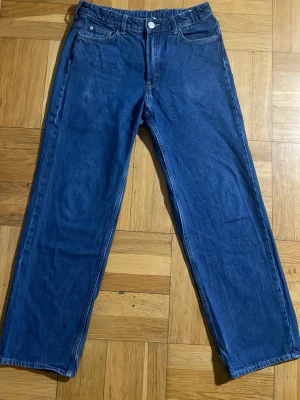 Blå raka jeans med hög midja - Snygga blå jeans med rak passform och hög midja. Klassisk femficksmodell med knapp och dragkedja framtill. Jeansen är tillverkade i denim och har en tidlös look som passar till det mesta. Perfekta för dig som gillar en enkel och clean stil.