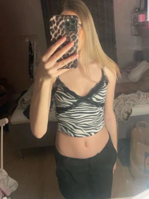 Zebramönstrad croppad linnetopp - Snygg zebramönstrad croppad linnetopp med svarta spetsdetaljer längs v-ringningen. Tunt axelbandslinne i svartvitt, perfekt för att sticka ut. Trendig och bekväm passform.