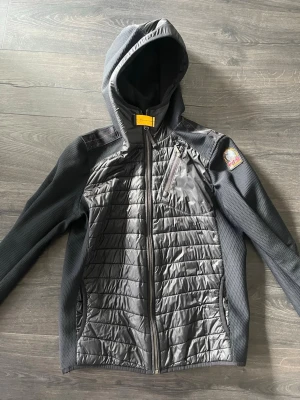 Svart jacka från Parajumpers - Snygg svart cardigan från Parajumpers med coolt patch på axeln och orange detalj. Jackan har meshfoder och är perfekt för kyligare dagar. Modellen heter Warm Up och har en sportig look. Den har nu blivit för liten. Passar dig som är 164-170 cm lång. Storleken är Youth large. Pris ej hugget i sten, hör av er vid funderingar! Nypris 4000kr