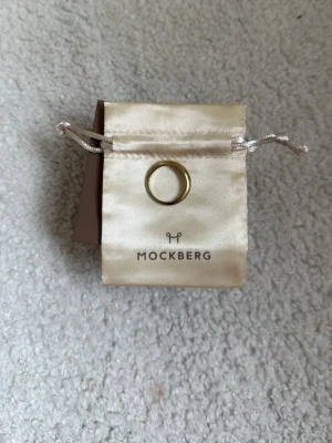 Guldfärgad ring från Mockberg classic  - Snygg och stilren guldfärgad ring från Mockberg. Ringen har en klassisk, slät design och levereras i en elegant beige tygpåse med Mockberg-logga. Perfekt accessoar för dig som gillar minimalistisk och tidlös stil. Storlek #54