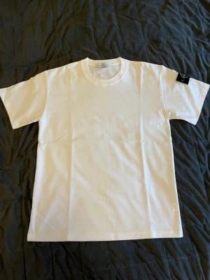 Vit t-shirt från Stone Island  - Helt ny vit t-shirt från Stone Island med rund hals och korta ärmar. Tillverkad i mjuk bomull för en skön känsla och enkel stil. Perfekt att matcha med jeans eller shorts för en clean look.