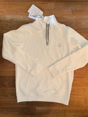 Vit half zip hoodie från Moncler - Snygg vit hoodie från Moncler med half zip-dragkedja och hög krage. Tröjan har lång ärm och Moncler-logga på bröstet. Perfekt för dig som gillar stilrena och exklusiva plagg. Tillverkad i mjuk bomull för maximal komfort.