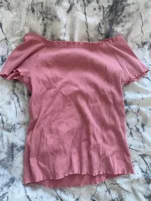 Rosa ribbad offshoulder topp - Söt rosa offshoulder topp med ribbad struktur och korta ärmar. Perfekt för varma dagar och enkel att styla med jeans eller kjol. Materialet känns mjukt och följsamt mot huden.