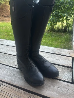 Svarta ridstövlar i läder - Säljer ett par svarta ridstövlar från Mountain Horse ( ridstövlar veganza svarta 38 short/regular.  De har snörning framtill, dragkedja på sidan och en klassisk hög modell som passar perfekt till ridning. Stövlarna har en stilren look och diskret logga upptill.