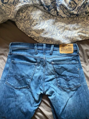 Blå jeans från Replay - Snygga blå jeans från Replay med klassisk femficksdesign och raka ben. Jeansen har en tydlig Replay-lapp bak i midjan och detaljerade sömmar på bakfickorna. Tillverkade i denim med en lätt tvättad look och silverfärgade nitar.