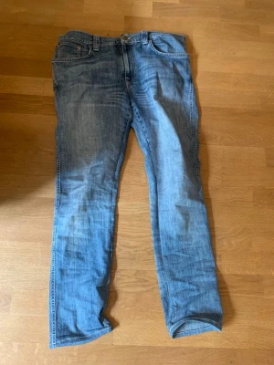 Ljusblå raka jeans - Säljer ett par ljusblå jeans från nuddie jeans med rak passform och klassisk femficksdesign. Jeansen har normal midja och är tillverkade i denim med lätt tvättad look. Perfekta för en avslappnad stil och passar till det mesta i garderoben.