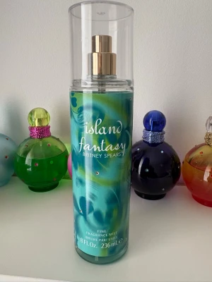 Britney Spears Island Fantasy Fragrance Mist 236 ml - Cirka 220–225 ml kvar i flaskan (se bilder för innehållsnivå). En fräsch och tropisk doft med saftiga citrusfrukter, klementin, röda bär och vattenmelon. De fruktiga tonerna balanseras av mjuka blomnoter och jasmin, medan mysk ger en lätt och feminin avslutning. Perfekt för dig som tycker om somriga, fruktiga och uppfriskande dofter.