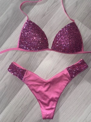 Rosa bikini med paljetter - Supersnygg rosa bikini med trekants-bh och matchande trosa. Både överdelen och sidorna på underdelen är täckta med glittriga paljetter för extra wow-effekt. Knytband i midja och nacke för justerbar passform. Bikinin är fåtal gånger använd och ser ut som ny. Överdel storlek 38 och underdel storlek 36.