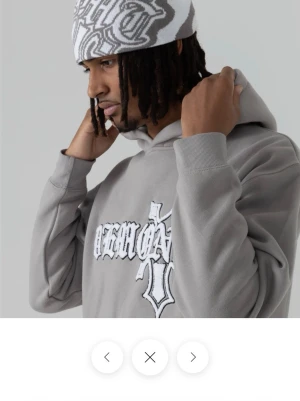 Grå hoodie från Delmont med tryck - Slut såld på hemsidan original pris 999kr men jag säljer för 799 Snygg grå hoodie från Delmont med stort vitt och svart tryck på bröstet i gotisk stil. Klassisk passform med huva och känguruficka framtill. Tillverkad i mjukt material som känns skönt mot huden. 