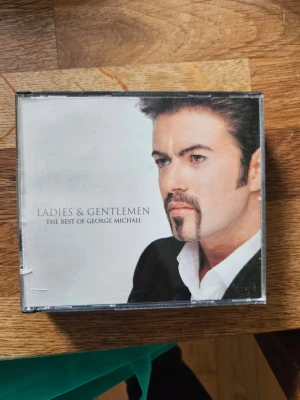 George Michael CD Ladies & Gentlemen - Säljer CD-albumet 'Ladies & Gentlemen: The Best of George Michael'. Omslaget är vitt med svart text och ett foto på George Michael. Albumet innehåller flera av hans största hits och kommer i ett klassiskt plastfodral.