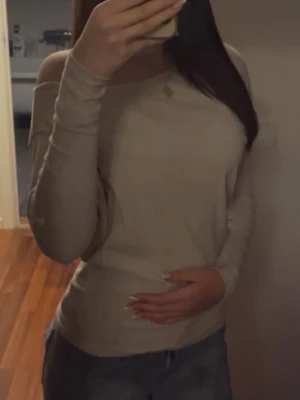 Beige offshoulder topp - Snygg beige offshoulder topp med lång ärm och figurnära passform. Perfekt att styla med jeans eller kjol för en trendig look. Enkel och stilren design utan synliga detaljer eller mönster.