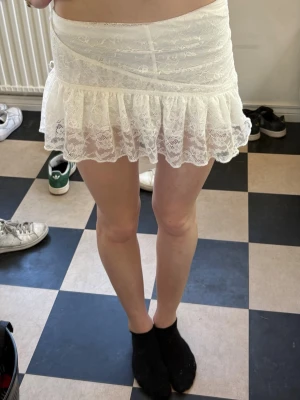 Vit spetskjol med volang - Söt vit kortkjol i spets med volangkant. Kjolen har en omlott-look upptill och är gjord i ett tunt, genomskinligt material som ger en romantisk vibe. Perfekt att styla med en enkel topp för en trendig look.💕💕