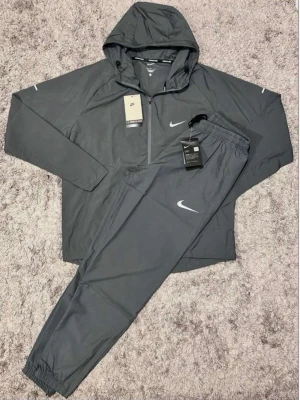 Nike Miller Track Suit Grå – Storlek S - Säljer en helt ny Nike Miller Track Suit i grå färg, storlek S. Setet består av en lätt jacka med huva och matchande byxor. Perfekt för träning, löpning eller en sportig vardagsstil. 