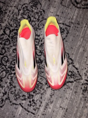 Adidas X Speedflow+ vita fotbollsskor - Säljer ett par Adidas X Speedflow+ fotbollsskor i vitt med svarta och röda detaljer samt gula inslag. Skorna är Fg, inga konstigheter på dobbarna, skorna är i använda skick, men ser bra ut om man rengör de