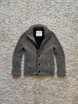 Hollister grå stickad fodrad kofta/cardigan  - Sjukt snygg jacka/kofta från hollister. Den är fodrad och varm o kan användas både som jacka över en hoodie eller endast som tröja när det blir varmare. Den är använd men i toppskick, storlek S. Tveka inte på o skriva vid fler frågor! Längd: 65 Bröstvidd: 50 Ärm: 66